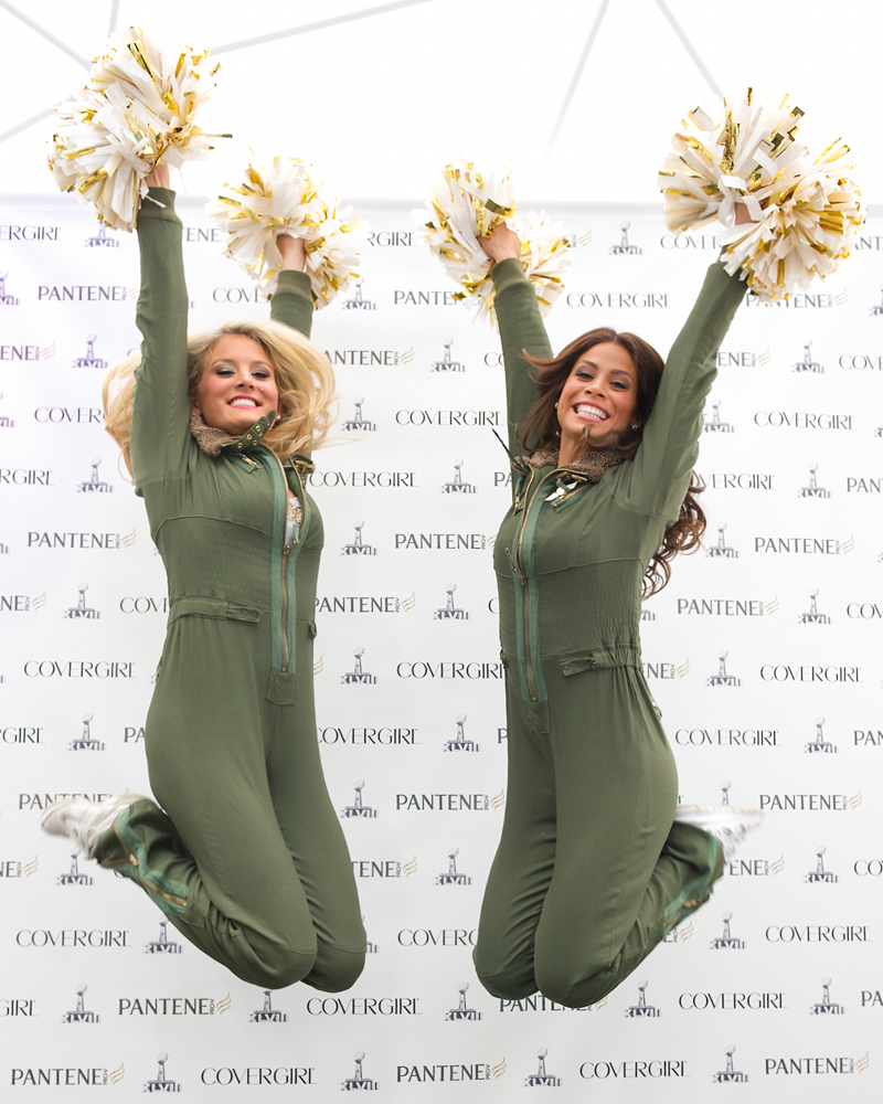 Two cheerleaders jumping with gold pom poms at a Super Bowl sponsor event